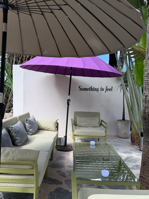 Modern patio seating area with lime green furniture, purple umbrellas, and white wall displaying Something to feel text