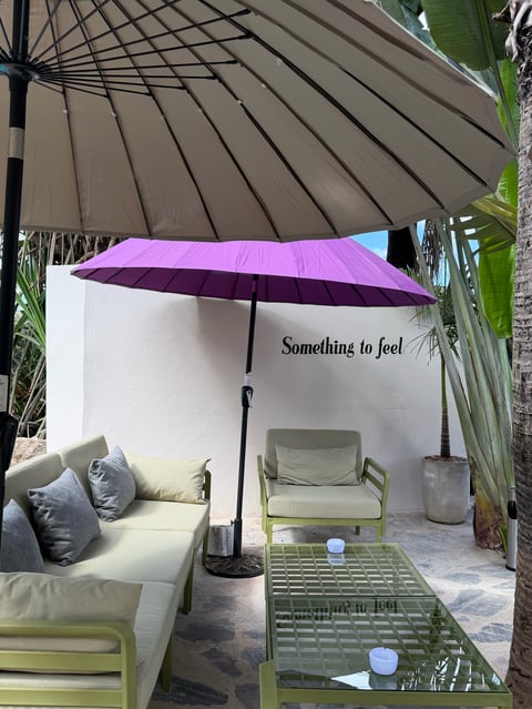 Outdoor lounge area with white walls, green furniture, purple umbrella, and text reading Something to feel